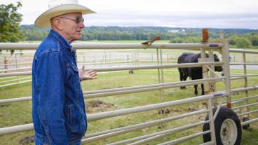 Eldon Cole standing in front of a field with a cow